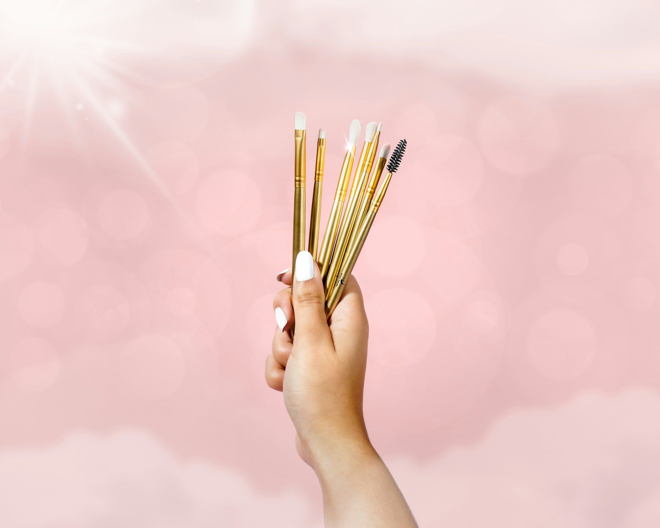 Eine Hand hält Bürstchen für Augenbrauen und Wimpern vor rosa Grund